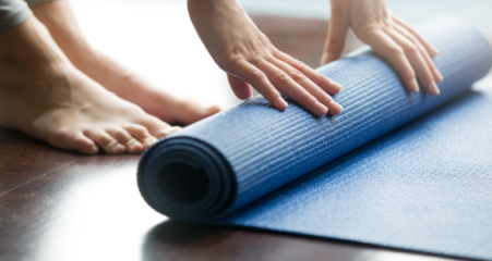 Ihmisen jalat ja kädet, jotka rullaavat joogamattoa kasaan.